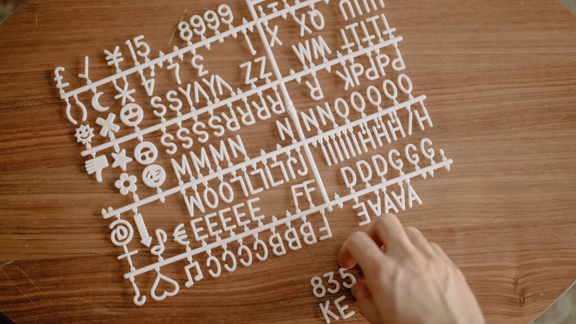 Een hand legt witte 3D-geprinte letters en cijfers op een houten letterbord