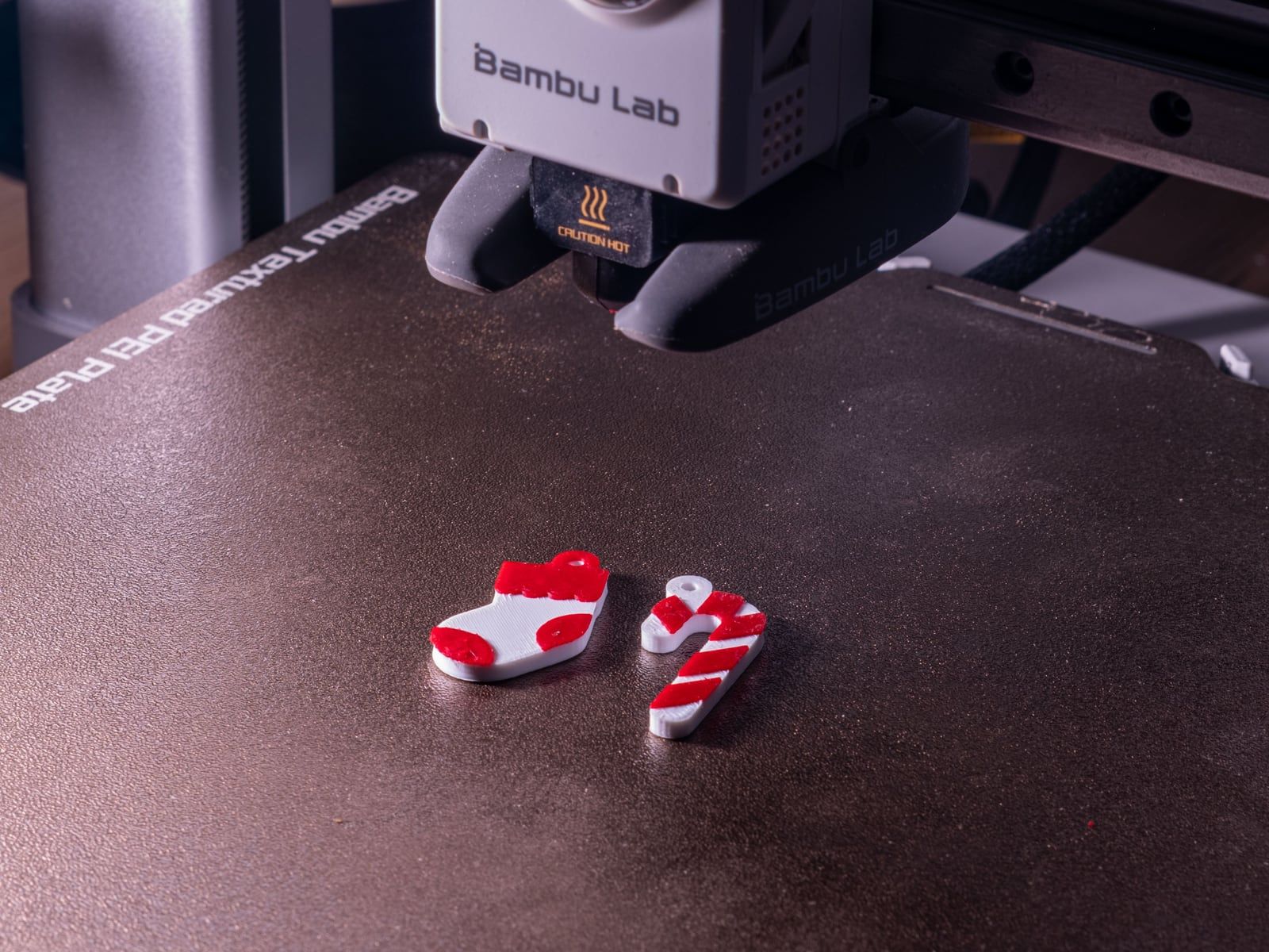 Twee rood-witte 3D-geprinte kersthangers op het printbed onder de printkop