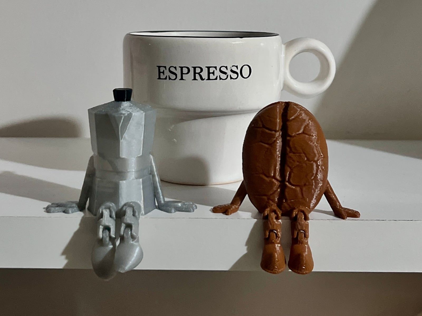 Twee 3D-geprinte figuurtjes, een moka-potje en een koffieboon, naast een espressokopje